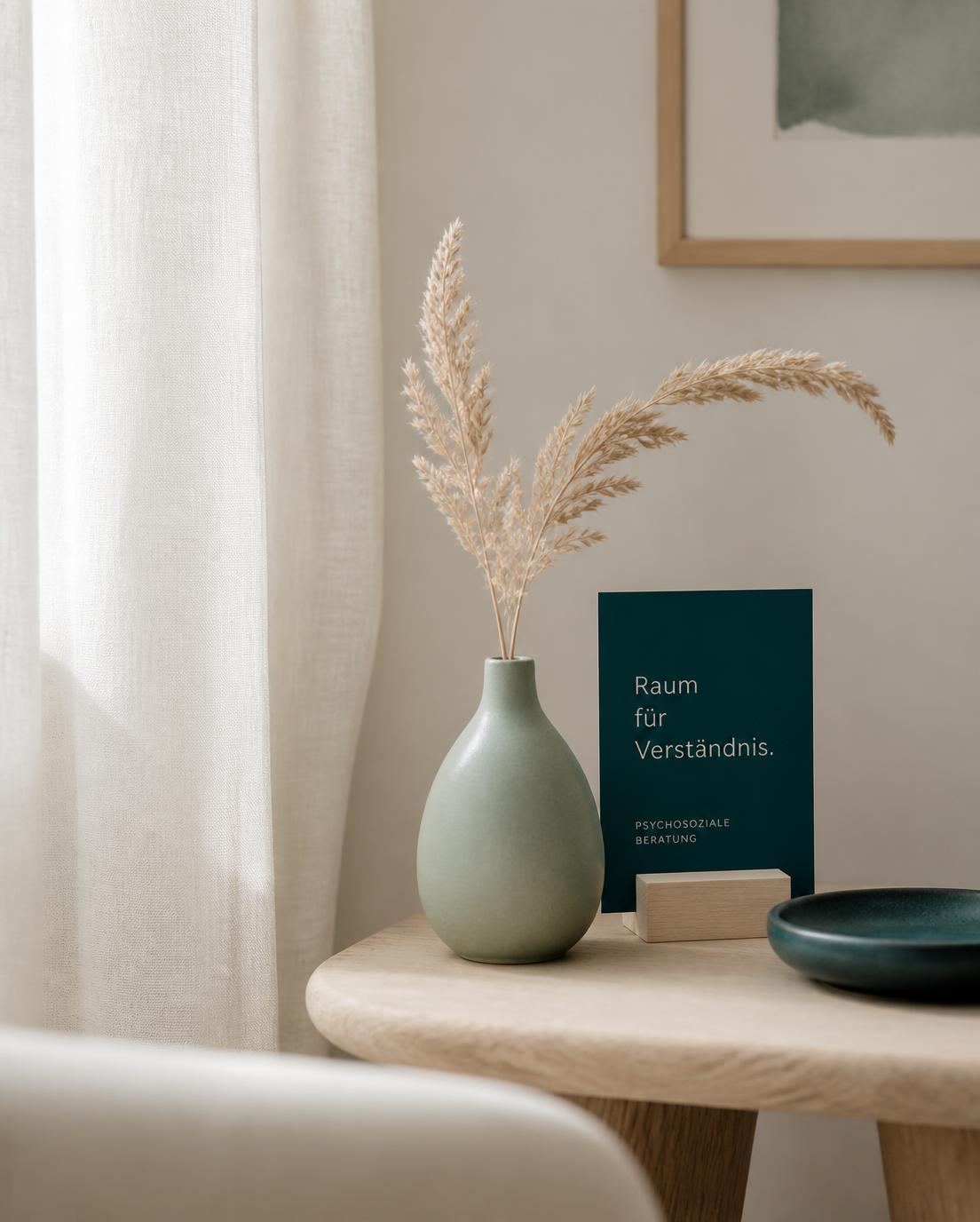 Stimmungsvolles Detail aus dem Beratungsraum: Vase mit Trockengras, sanftes Tageslicht und gedämpfte Petrol-Akzente